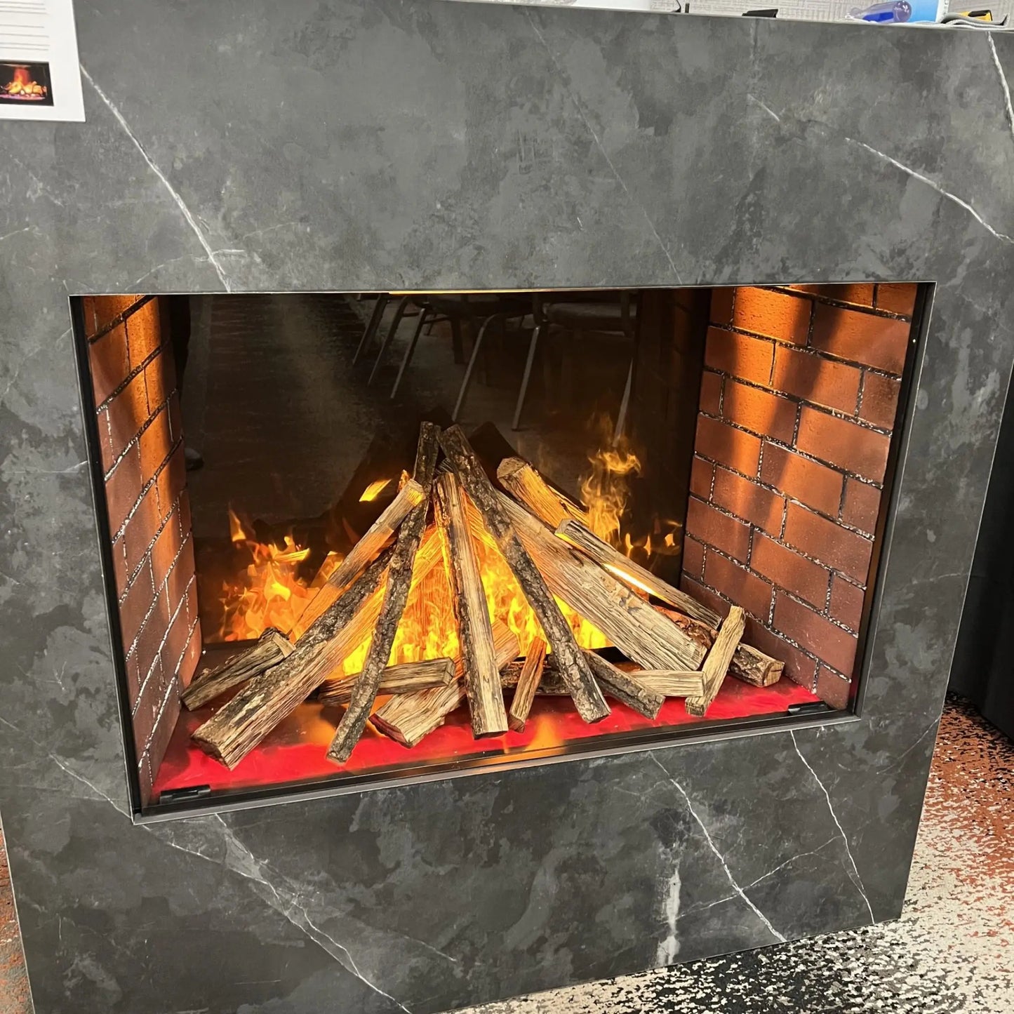 Close-up studio product photo of the built-in electric fireplace insert framed in dark marble-look surround, showing the log set and orange flame effect in detail.