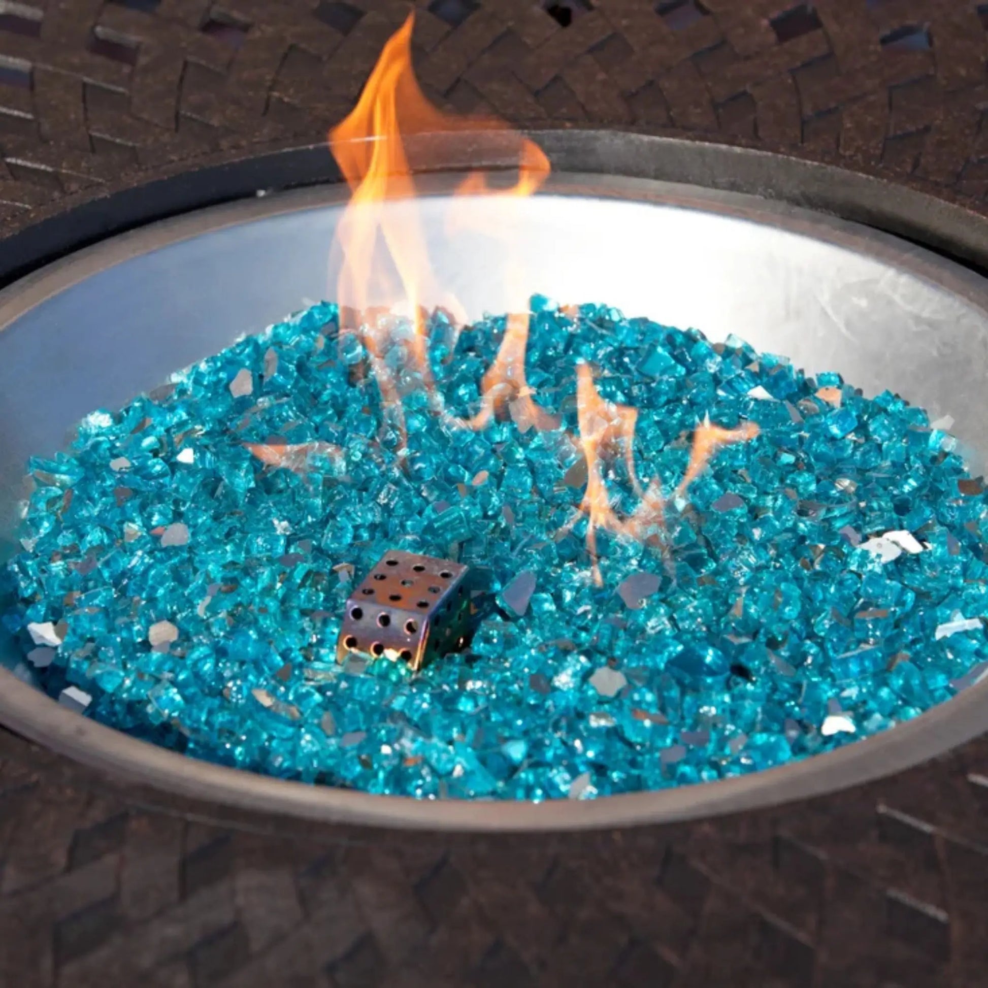 Blue glass fire stones in a round metal fire pit bowl with orange flames burning, and a small metal wind guard.