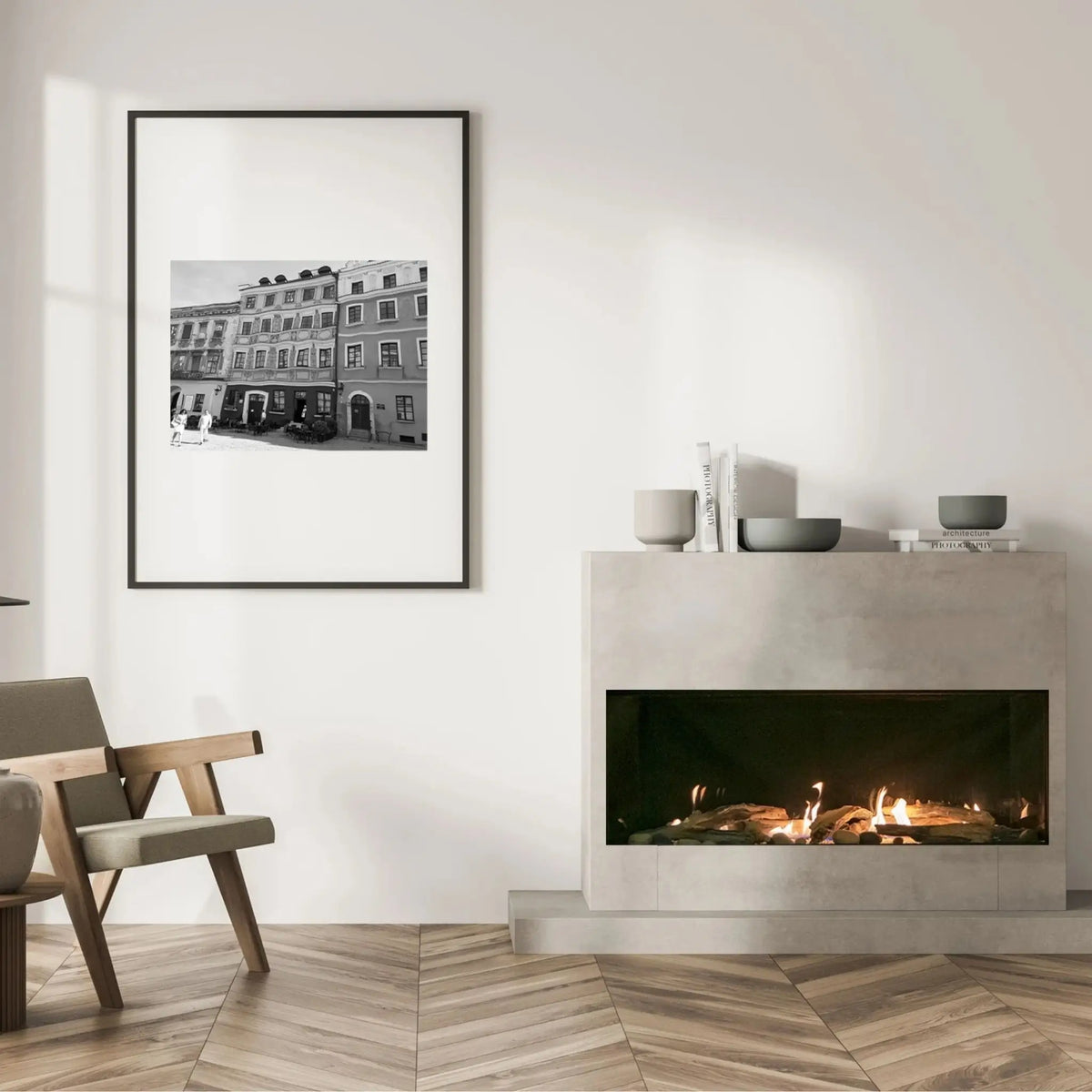 A framed black and white architectural photograph of a historic building hangs on a white wall in a modern living room setting with a fireplace, wooden floor, and a chair.