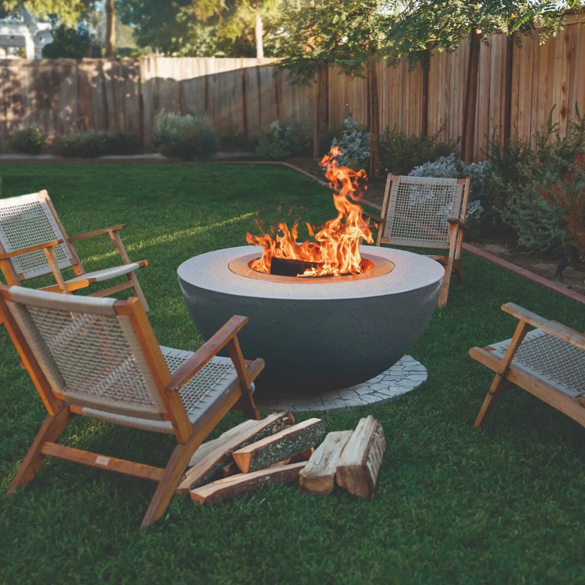 LUME Surround 1 smokeless wood-burning fire pit in a backyard with outdoor chairs and stacked firewood