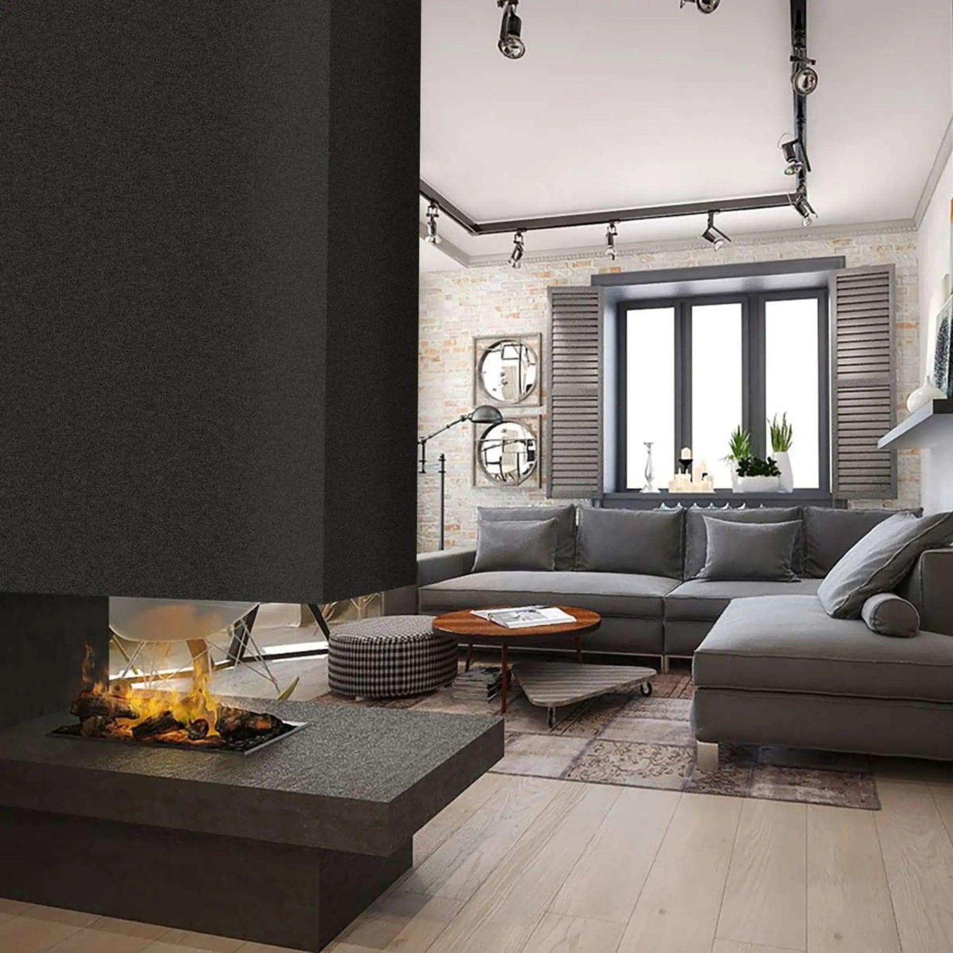 An Optimyst water vapor cassette installed in a dark two-sided room-divider fireplace with a stone hearth, shown burning in a modern living room with a gray sectional sofa, round mirrors, and industrial track lighting.