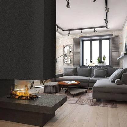 An Optimyst water vapor cassette installed in a dark two-sided room-divider fireplace with a stone hearth, shown burning in a modern living room with a gray sectional sofa, round mirrors, and industrial track lighting.