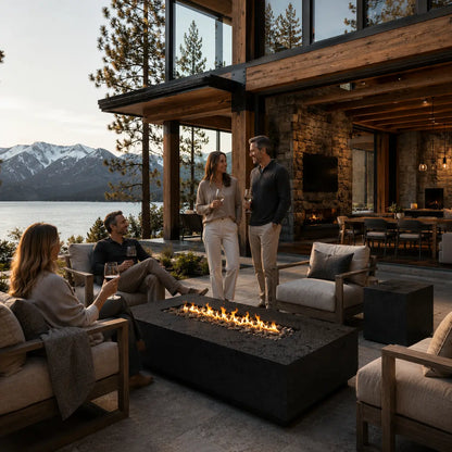 People socializing around a fire pit in a luxurious outdoor setting with mountains and water in the background.